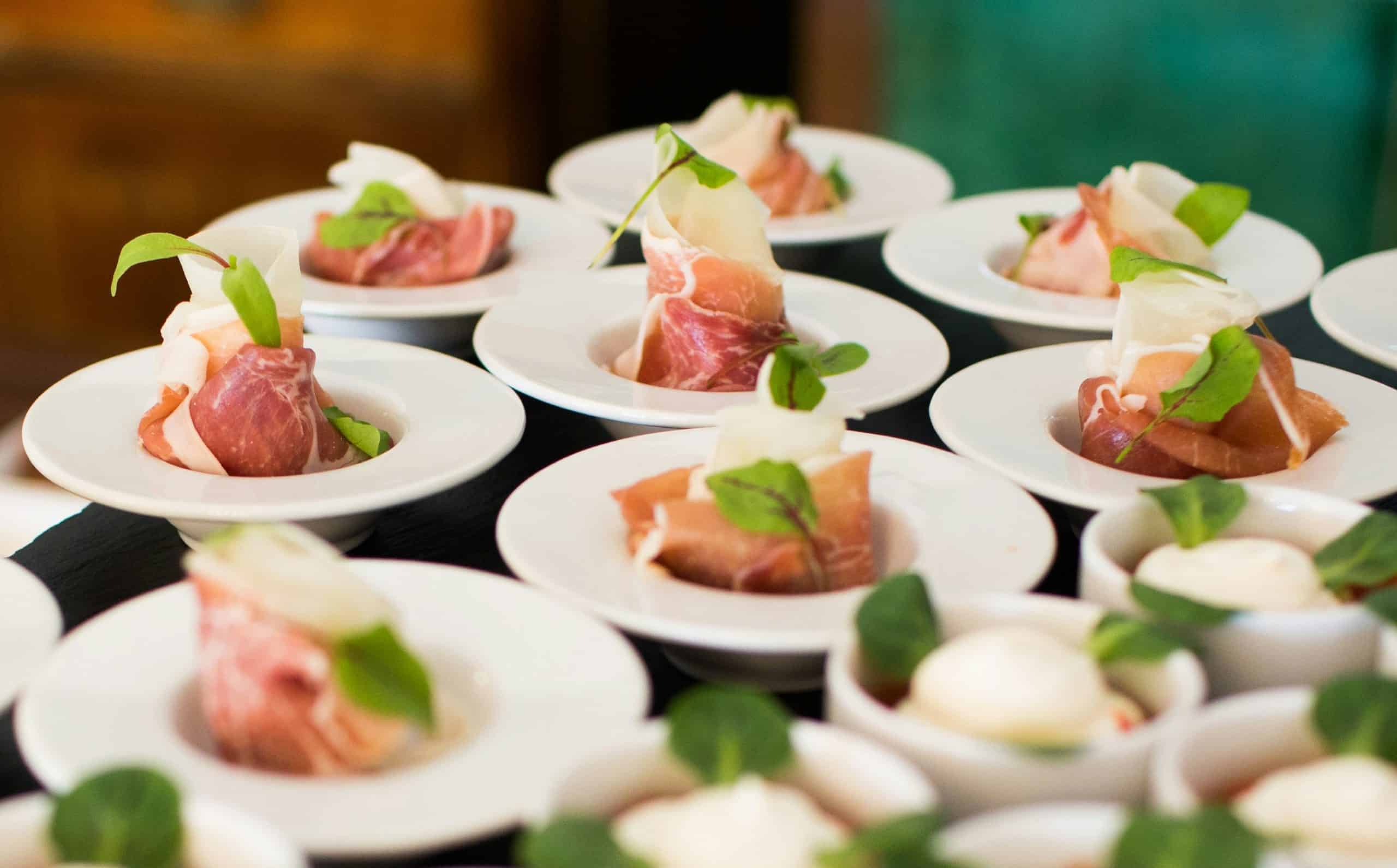 Mehrere Teller mit Rohschinken angerichtet auf weissen Tellern für den Catering-Service
